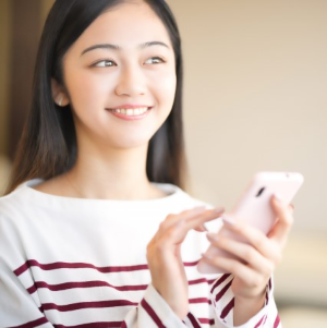 スマホを手にわざと既読を遅らせ、素っ気ない表情を作っている女性。仮交際LINEで駆け引きしすぎるNGを表す写真アイコン - はなまるプロ