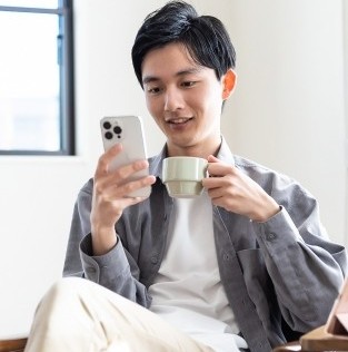 自宅のソファでスマホからオンライン結婚相談所を比べる30代男性｜店舗型との違い - はなまるプロ